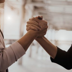 Two women shaking hands in a professional setting, symbolizing partnership and collaboration, with a blurred background.